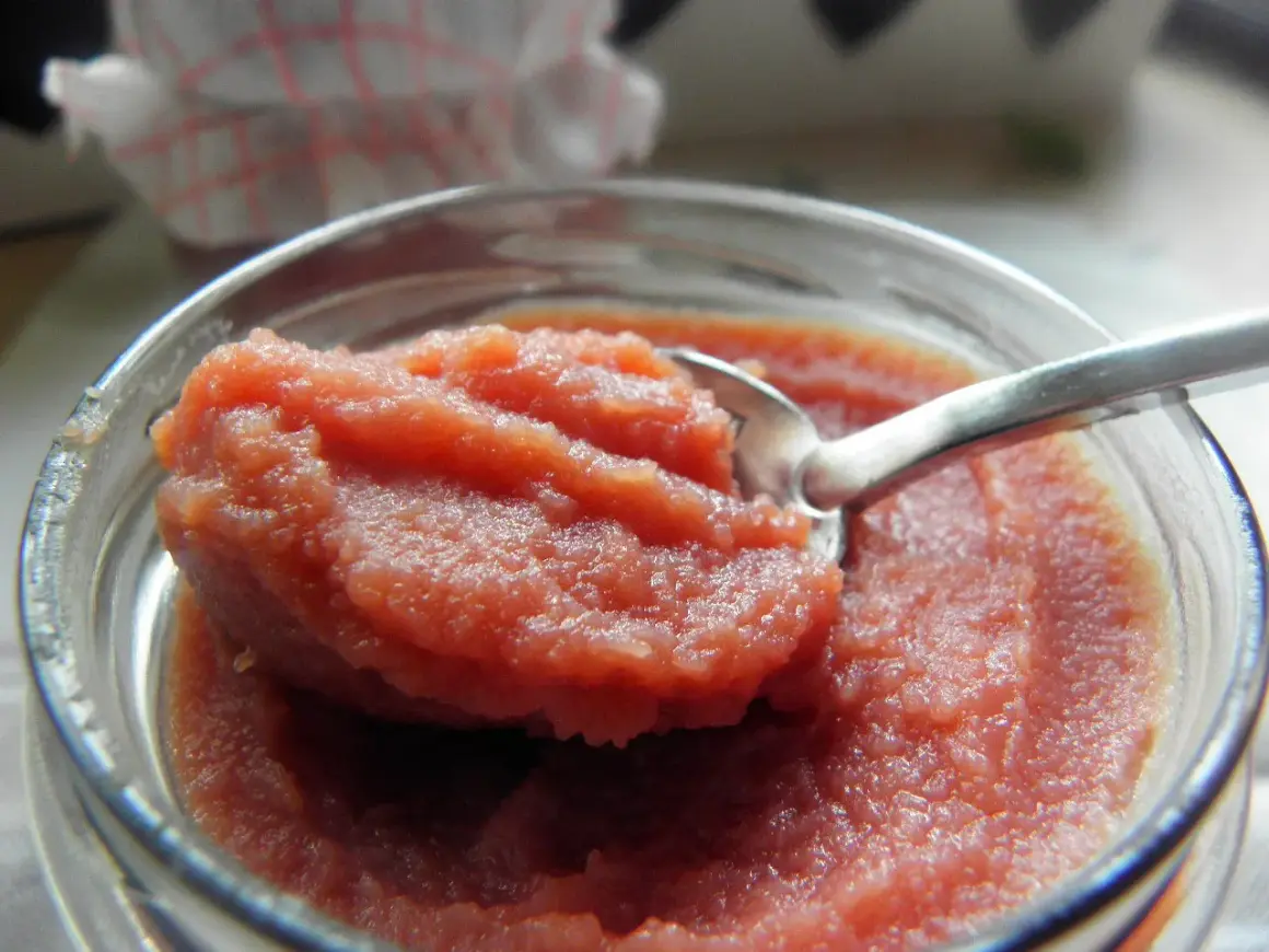 Łyżeczka zanurzona w słoiku z gęstym, różowym curd wiśniowym. Idealny dodatek do deserów.