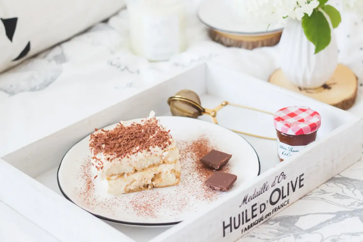 Pyszne tiramisu z biszkoptami, posypane kakao i czekoladą, na tacy z dżemem i kwiatami. Idealne na leniwe popołudnie.