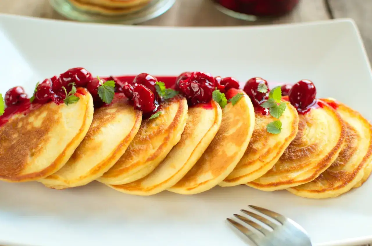 Puszyste pancakes na maślance, polane wiśniowym sosem i ozdobione listkami mięty. Idealne na słodkie śniadanie.