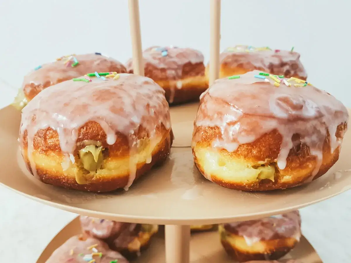 Pyszne pączki pistacjowe z lukrem i kolorową posypką, pięknie ułożone na paterze.