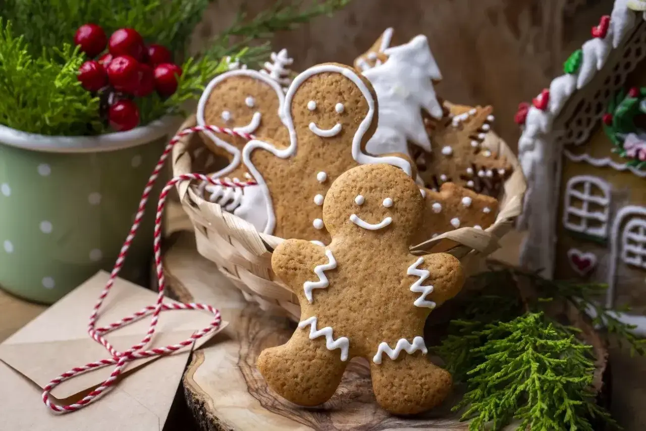 Koszyk pełen uśmiechniętych ciastek korzennych w kształcie ludzików i choinek, obok domku z piernika.