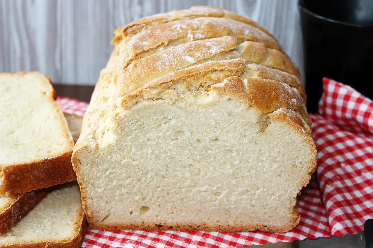 Szybki chleb z chrupiącą skórką i puszystym wnętrzem, idealny na śniadanie. Obok kromki świeżo upieczonego bochenka.