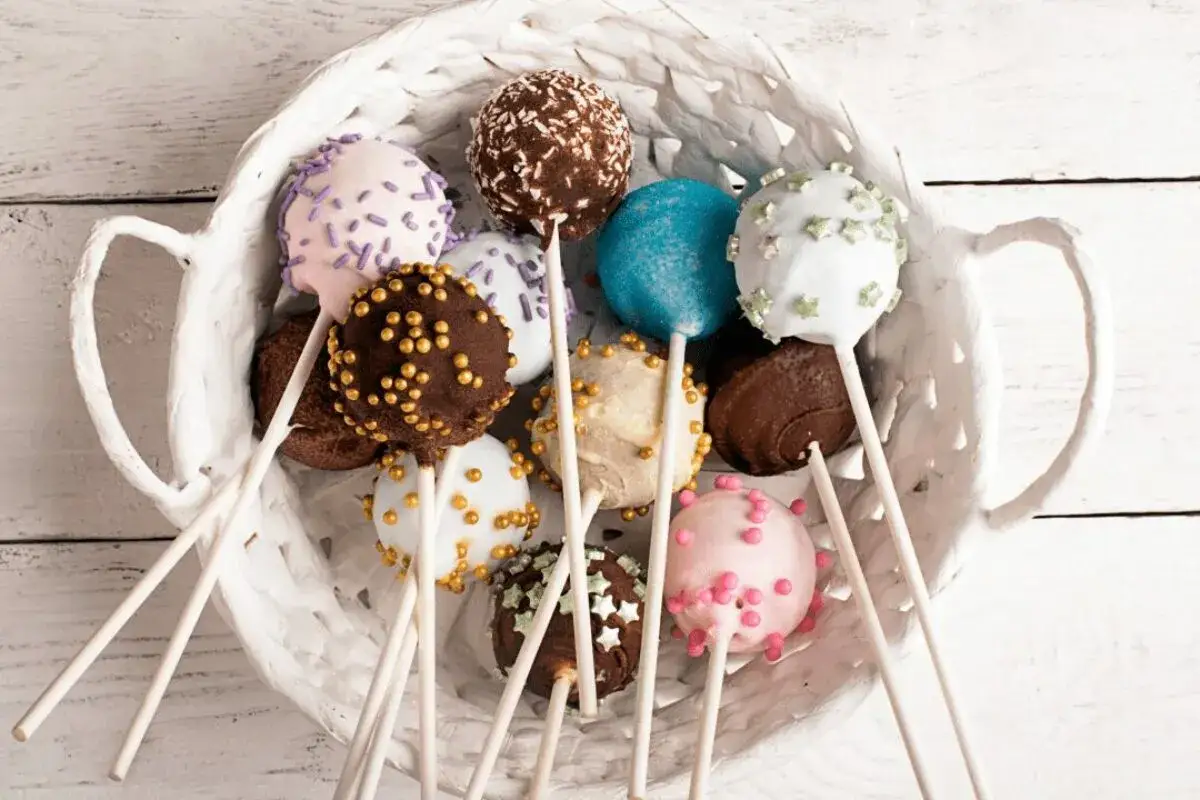 Kolorowe cake pops kokosowe w białym koszyku, ozdobione posypkami i kuleczkami.