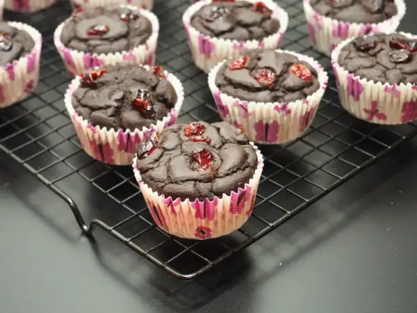 Czekoladowe muffinki z fasoli, ozdobione suszoną żurawiną, prezentują się apetycznie na czarnej kratce.