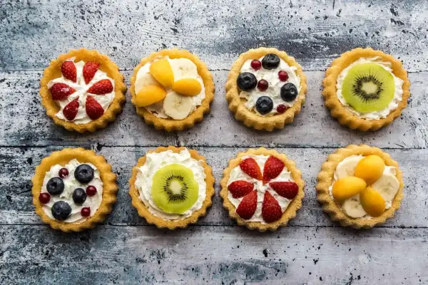 Kolorowe tartaletki z owocami: truskawki, kiwi, borówki, maliny i morele na kremowym nadzieniu.