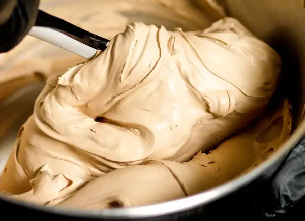 Gładka, kremowa masa o kolorze **salted caramel** jest mieszana łopatką w metalowej misce.