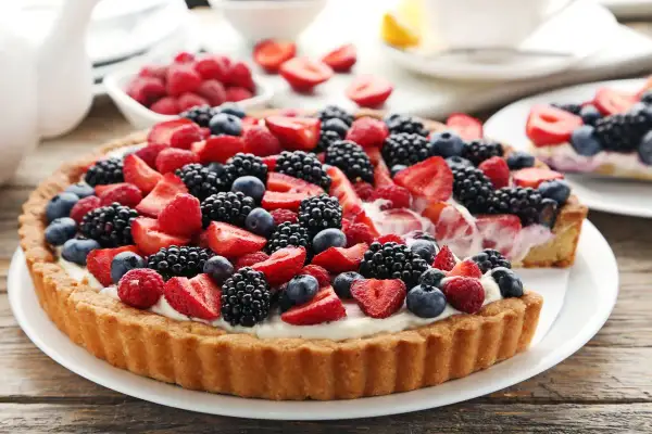Pyszna tarta z kremem patissiere, obficie udekorowana świeżymi malinami, borówkami, jeżynami i truskawkami.
