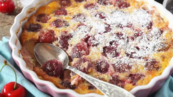 Pyszne clafoutis z wiśniami, posypane cukrem pudrem, czeka na łyżeczkę. Idealny deser na letnie popołudnie.