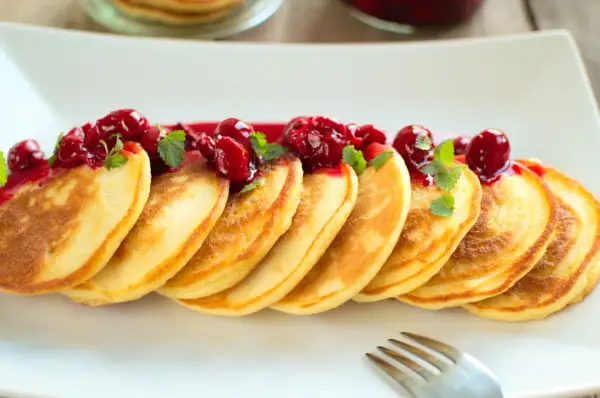 Puszyste pancakes na maślance, polane wiśniowym sosem i ozdobione listkami mięty. Idealne na słodkie śniadanie.