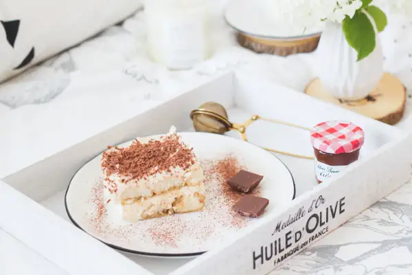 Pyszne tiramisu z biszkoptami, posypane kakao i czekoladą, na tacy z dżemem i kwiatami. Idealne na leniwe popołudnie.