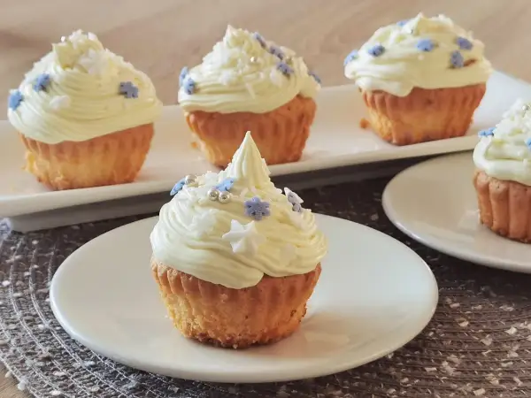 Pyszne muffinki z kremem w środku, ozdobione białym kremem i niebieskimi oraz białymi posypkami w kształcie gwiazdek i płatków śniegu.