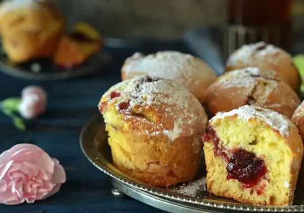 Puszyste muffinki z dżemem, posypane cukrem pudrem, kuszą swoim domowym wyglądem.